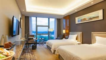 A hotel room with two beds, a desk with a chair, a TV, and a large window offering a view.