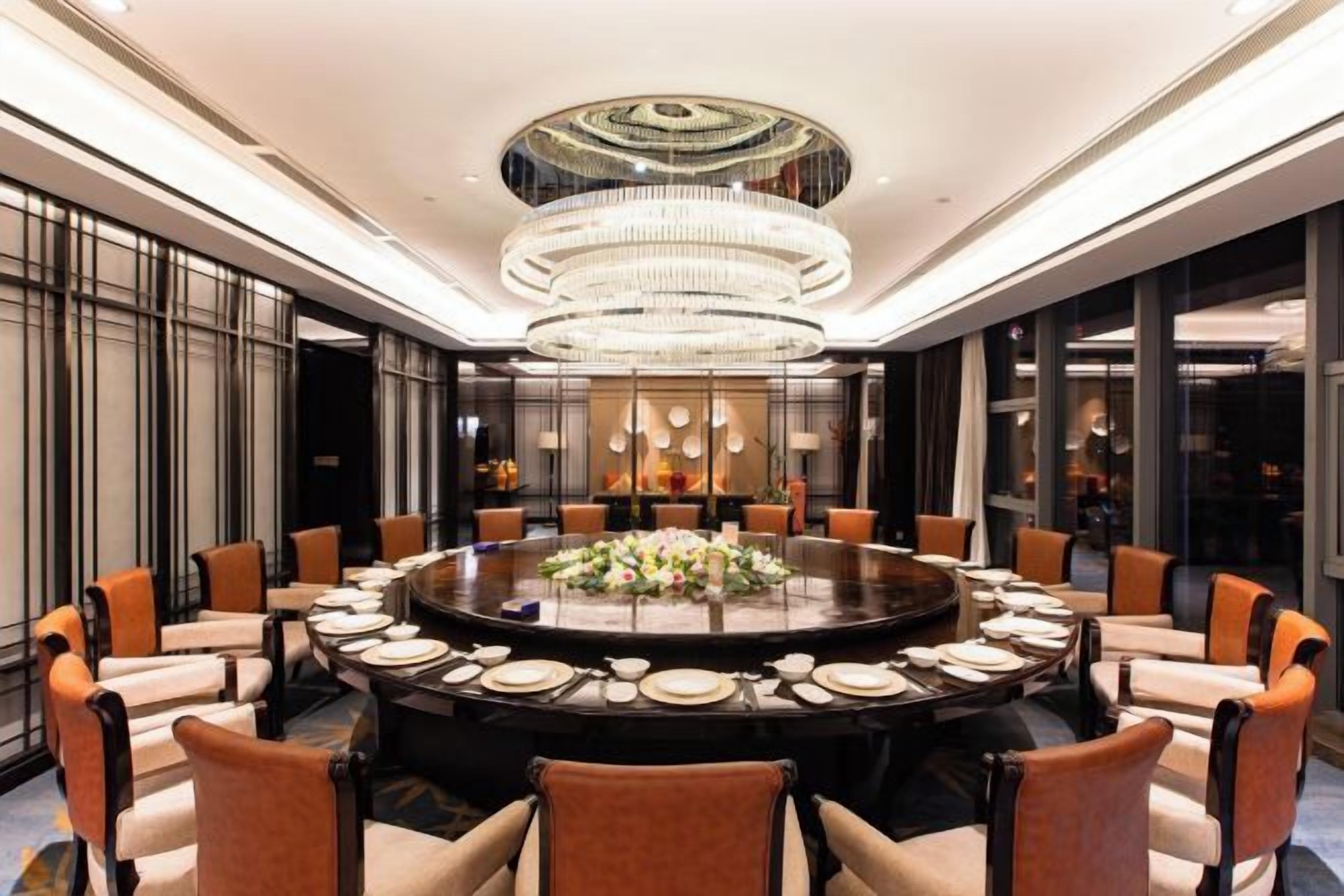 A round dining table with chairs, a chandelier, and a floral centerpiece.