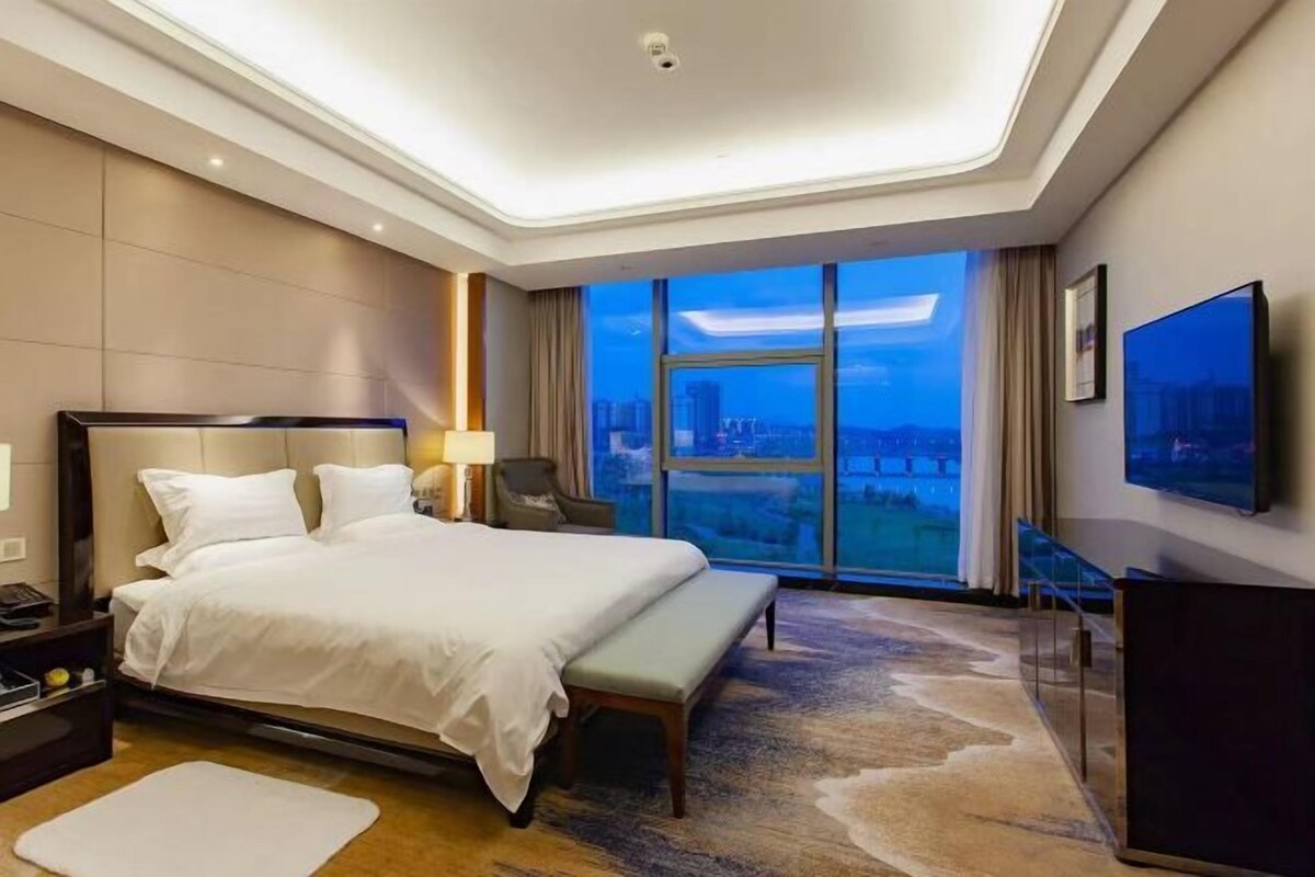 Habitación de hotel con una cama grande, un escritorio, una silla, un televisor y vistas a la ciudad.