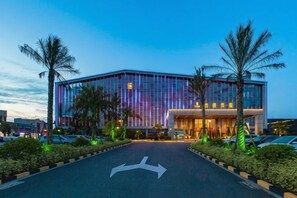 A modern hotel with a glass facade, a parking lot, and palm trees. - Hui Chang Hotel (Huichang)