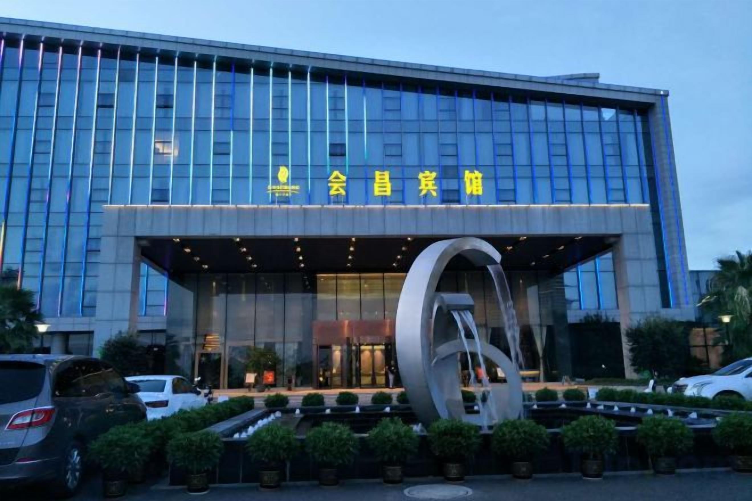 A modern building with a large glass facade and a prominent circular sculpture in front.