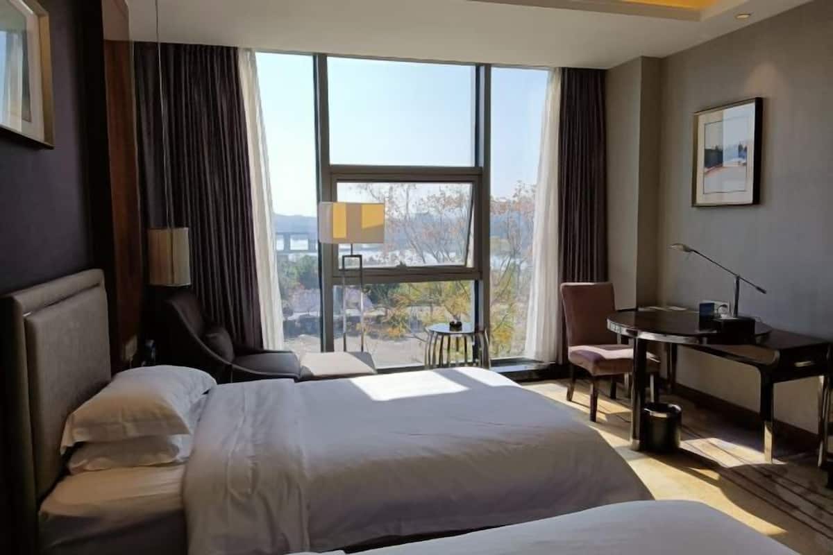 A hotel room with two beds, a desk, a chair, and a view of the outdoors.