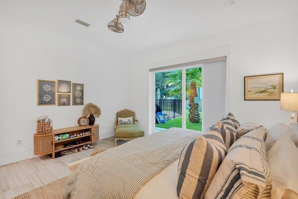 A bedroom with a bed, a wooden console table with shoes, a chair, and a view of greenery through a sliding door.