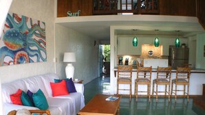 A spacious living area with a sofa, chairs, a coffee table, and a kitchen in the background. - Kraken Cove St. Croix (Sion Farm)