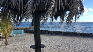 A beach with a thatched umbrella, a blue bench, and a rocky shoreline. - Kraken Cove St. Croix (Sion Farm)