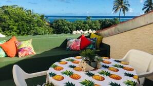 A beachside seating area with a table covered in a pineapple pattern, surrounded by colorful pillows and a small plant. - Kraken Cove St. Croix (Sion Farm)