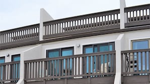 A modern multi-story building with balconies, large windows, and a sandy ground area with stepping stones.