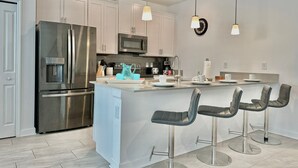 Una cocina moderna con electrodomésticos de acero inoxidable, armarios blancos y una isla central con taburetes de bar.