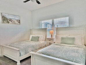 A bedroom with two single beds, a nightstand with a lamp, and a window with blinds.