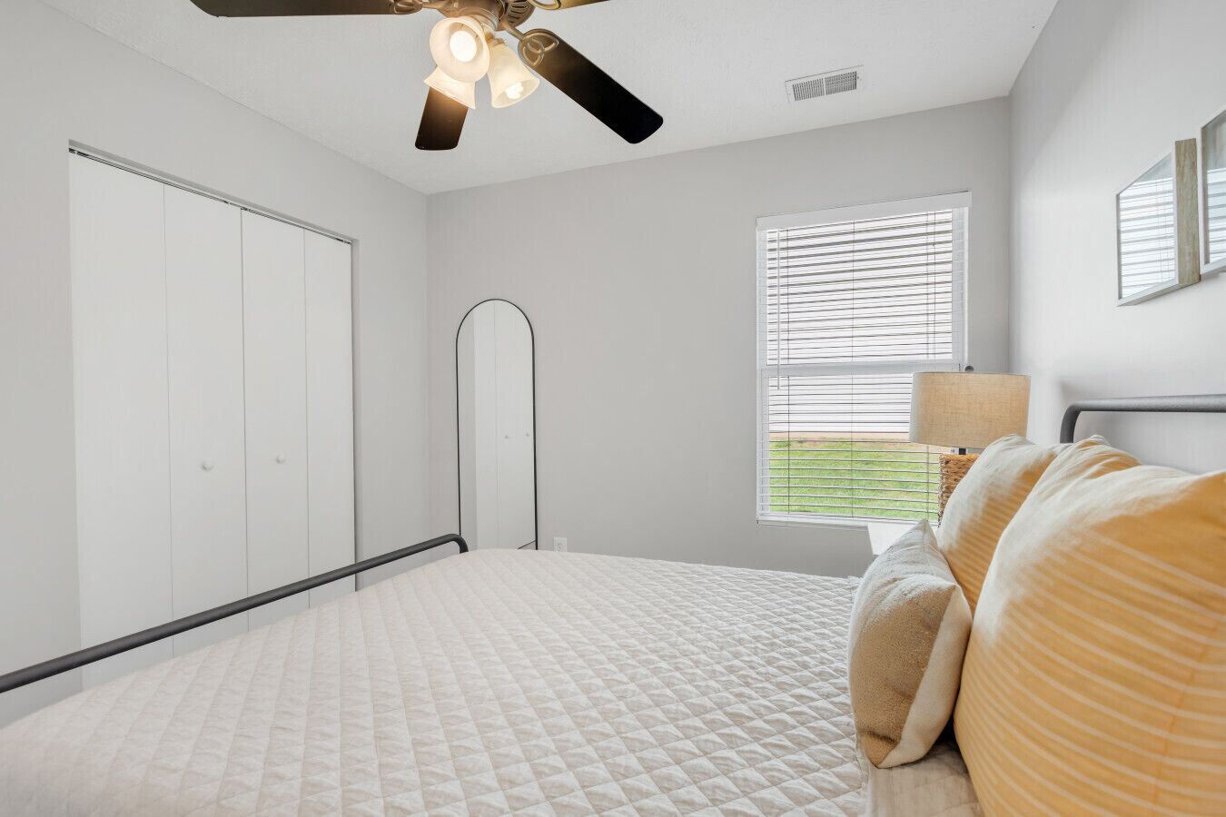 A bedroom with a bed, a ceiling fan, a window with blinds, and a wardrobe.