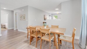 Un vaste espace dédié à la salle à manger, avec une table et des chaises en bois, des murs blancs et un plafond doté d’un éclairage encastré.