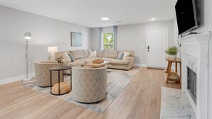 Un salon moderne avec un canapé d’angle, deux poufs, une lampe sur pied et une cheminée.
