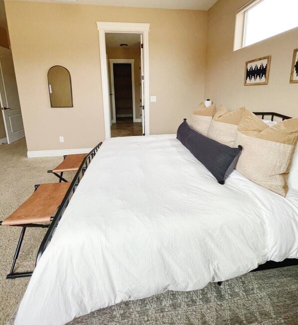 A bedroom with a large bed, a bench, a door, and a wall-mounted mirror.
