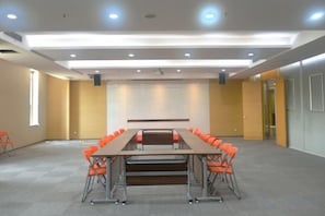 A conference room with a long table and orange chairs, a projector screen, and a carpeted floor.