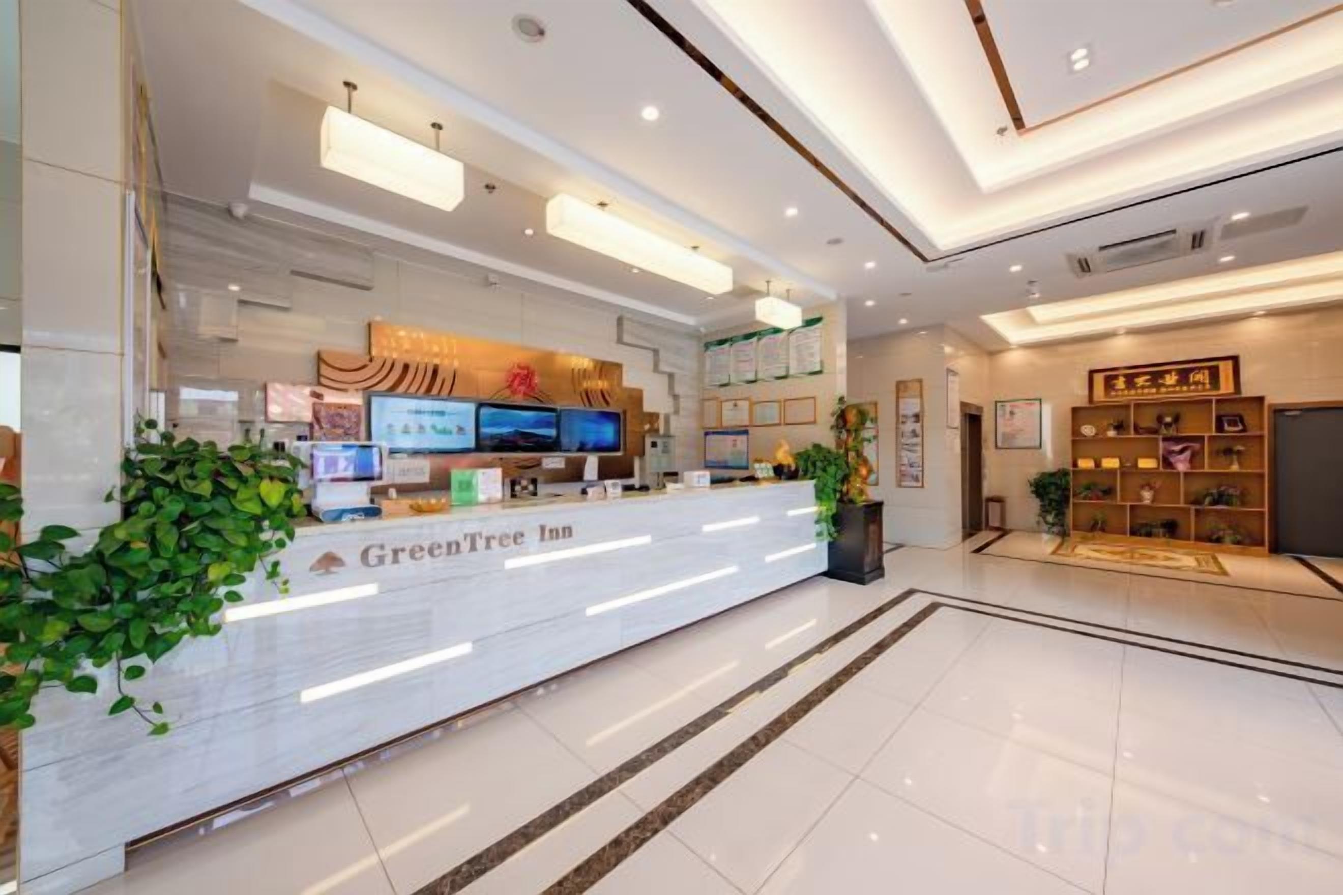 A hotel reception area with a reception desk, digital screens, and a plant.