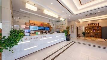 A hotel reception area with a reception desk, digital screens, and a plant.