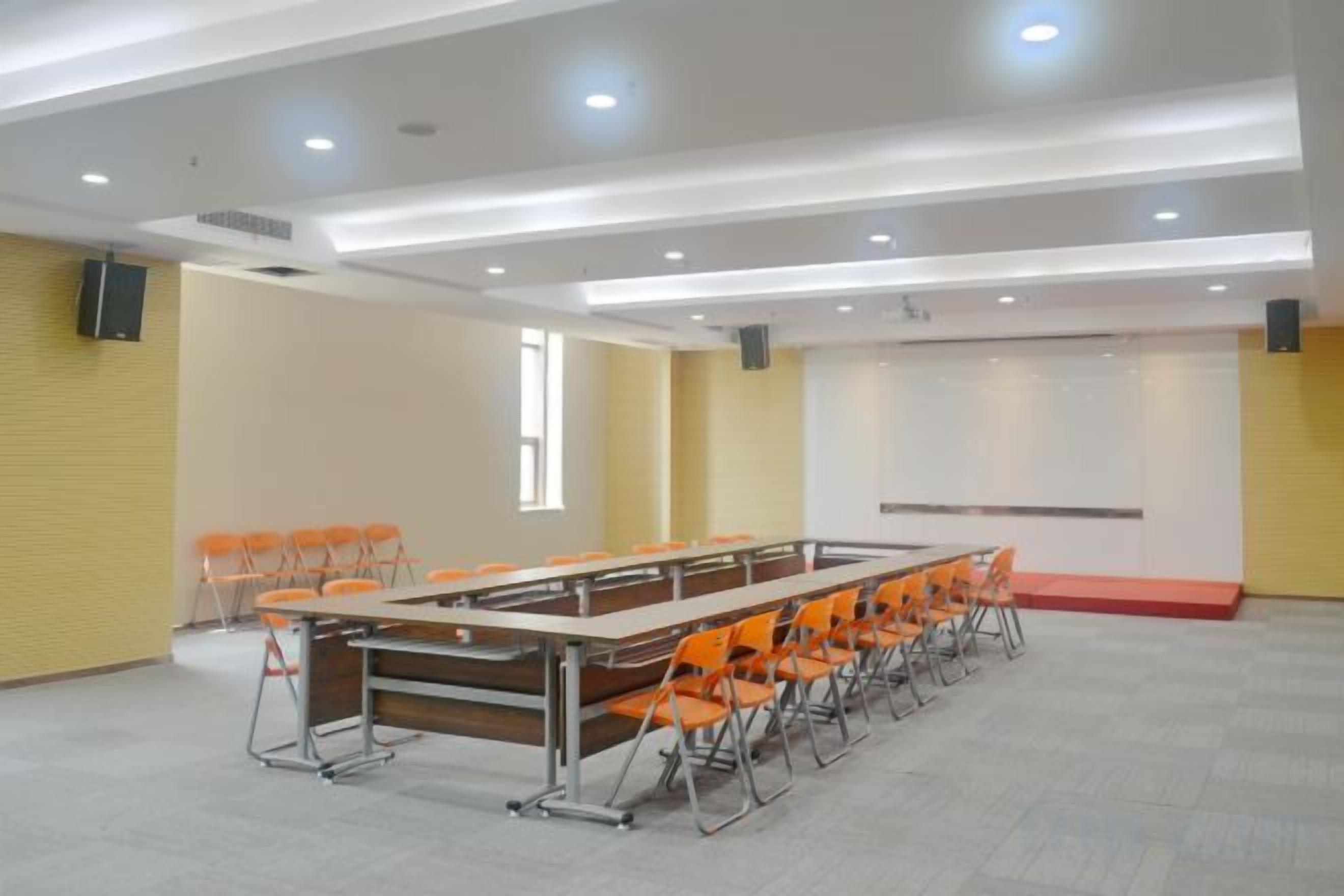 Un salón de conferencias con una larga mesa, sillas, una pizarra y una pantalla de proyector.