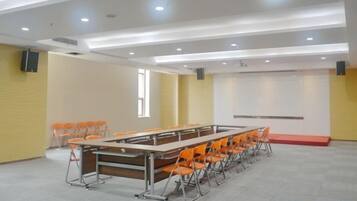 Un salón de conferencias con una larga mesa, sillas, una pizarra y una pantalla de proyector.