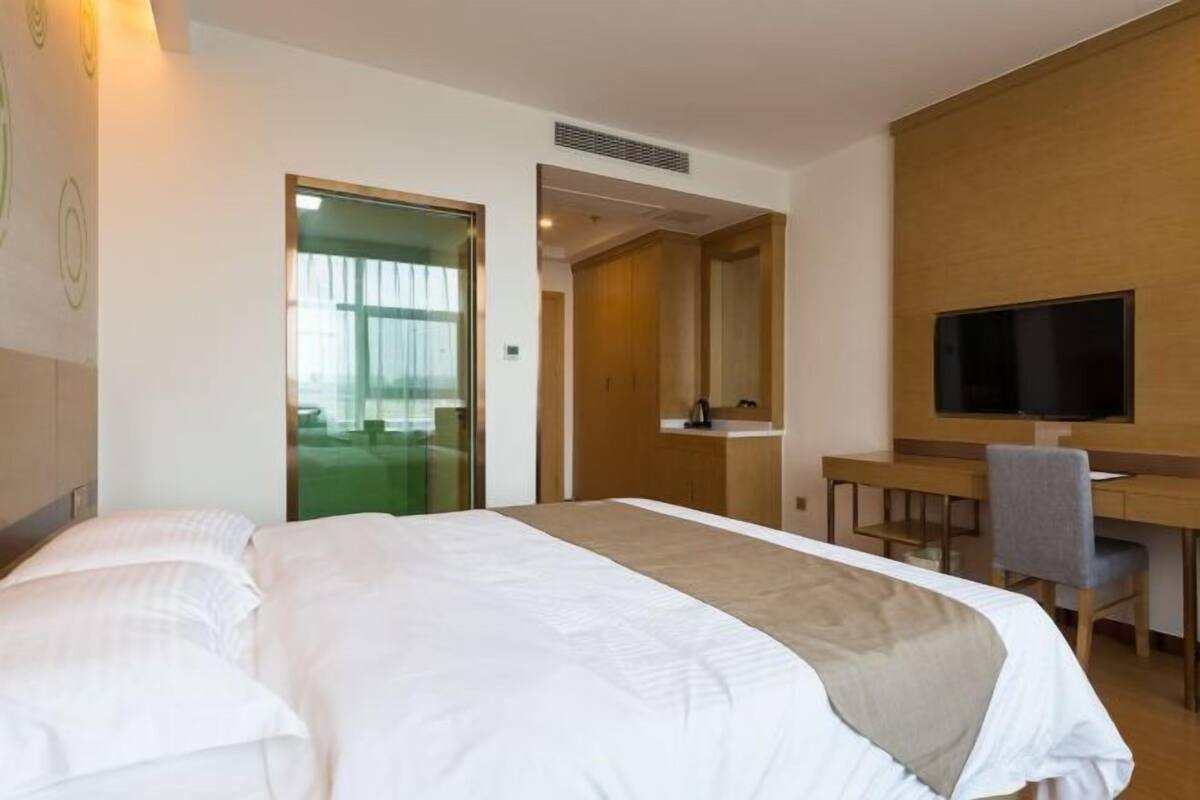A hotel room with a large bed, a desk with a chair, a television, and a mirror.