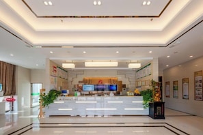 A hotel reception area with a modern design, featuring a reception desk, a flat-screen TV, and a digital information board.