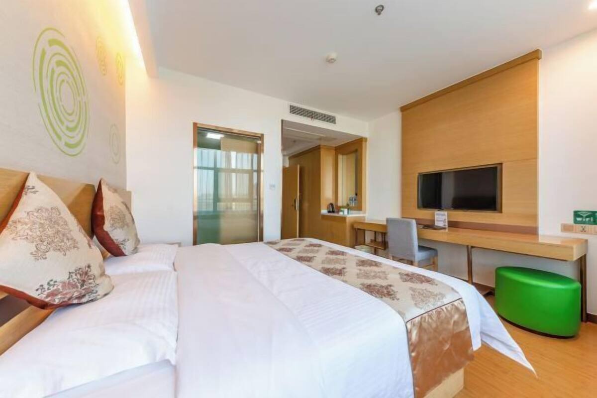A hotel room with a bed, a desk, a television, and a green ottoman.