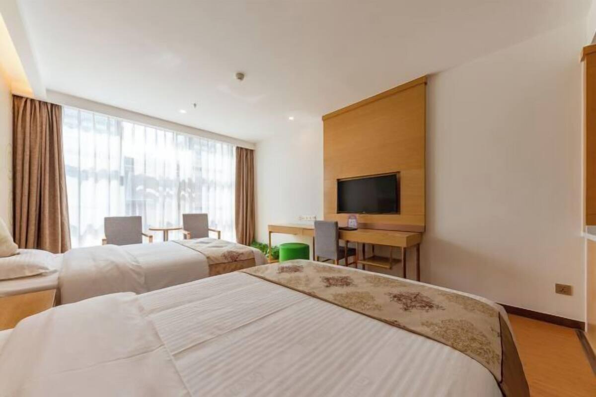 A hotel room with two beds, a desk, a chair, a television, and a large window.