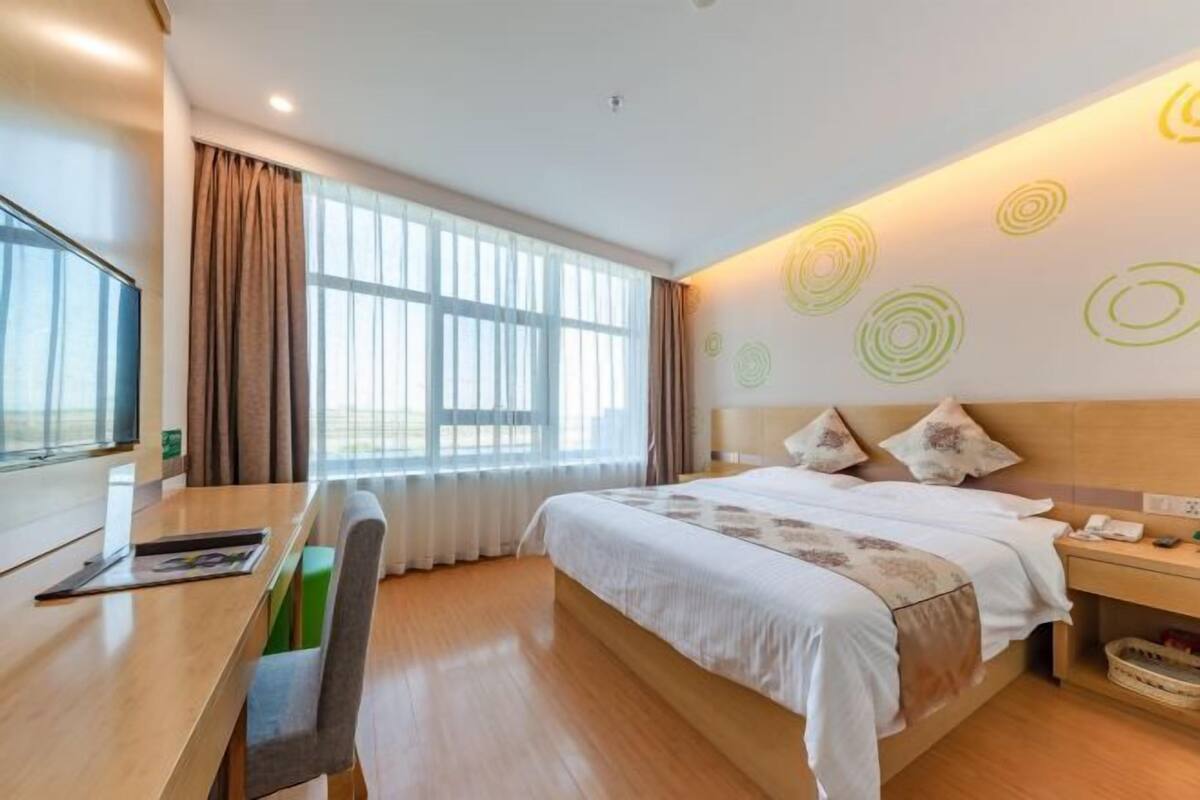 A hotel room with a bed, a desk, a chair, a TV, and a window with curtains.