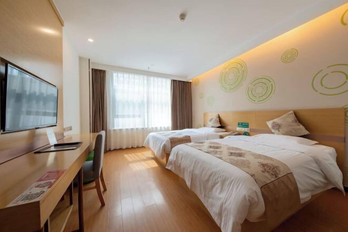 A hotel room with two beds, a desk, a chair, and a TV.