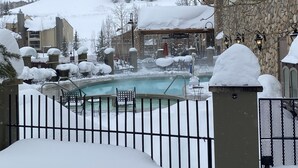 Ein mit Schnee bedeckter Poolbereich im Freien mit Liegestühlen und einem Steinhaus im Hintergrund.