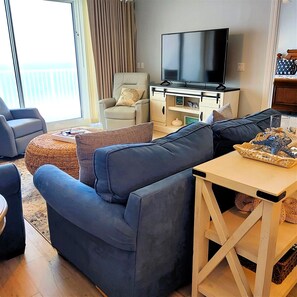 A modern living room with a large flat-screen TV, comfortable seating, and a view of the outdoors.