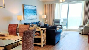 Ein modernes Wohnzimmer mit Essbereich, ausgestattet mit Korbstühlen, einem blauen Sofa und einem Glastisch.