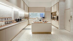 A modern hotel lobby with a central reception desk, a buffet area, and a seating area with a view of the cityscape. - Ji Hotel Shanghai Songjiang Sports Square Center (Shanghai)