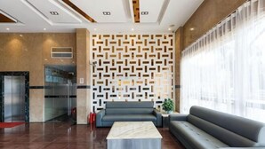 Eine moderne Lobby mit Wandmuster, einer Couch, einem Couchtisch und einem Glastreppenaufzug.