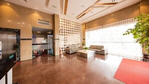 Eine moderne Lobby mit einem Marmor-Empfangstresen, einer Sitzecke mit Sofas, einer Wand mit Muster und einem großen Fenster mit transparenten Vorhängen.