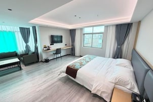Una habitación de hotel con cama, escritorio, silla, televisor y ventana.