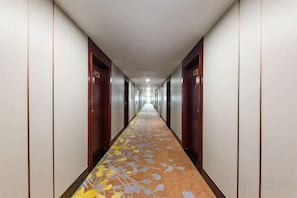 A hotel corridor with doors on both sides, a carpet with a leaf pattern, and a ceiling with recessed lighting. - wonder travel hotel(kaiping dongxing) (Kaiping)