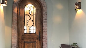 Una puerta de madera con un panel de vidrio, flanqueada por dos luces empotradas, un banco y una planta en maceta.