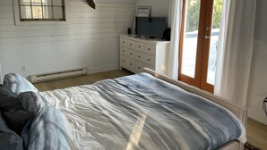 A bedroom with a bed, a dresser, a television on top, a window, and a door with curtains.