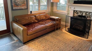 A living room with a brown leather sofa, a small white side table, a fireplace, and a television mounted on the wall.