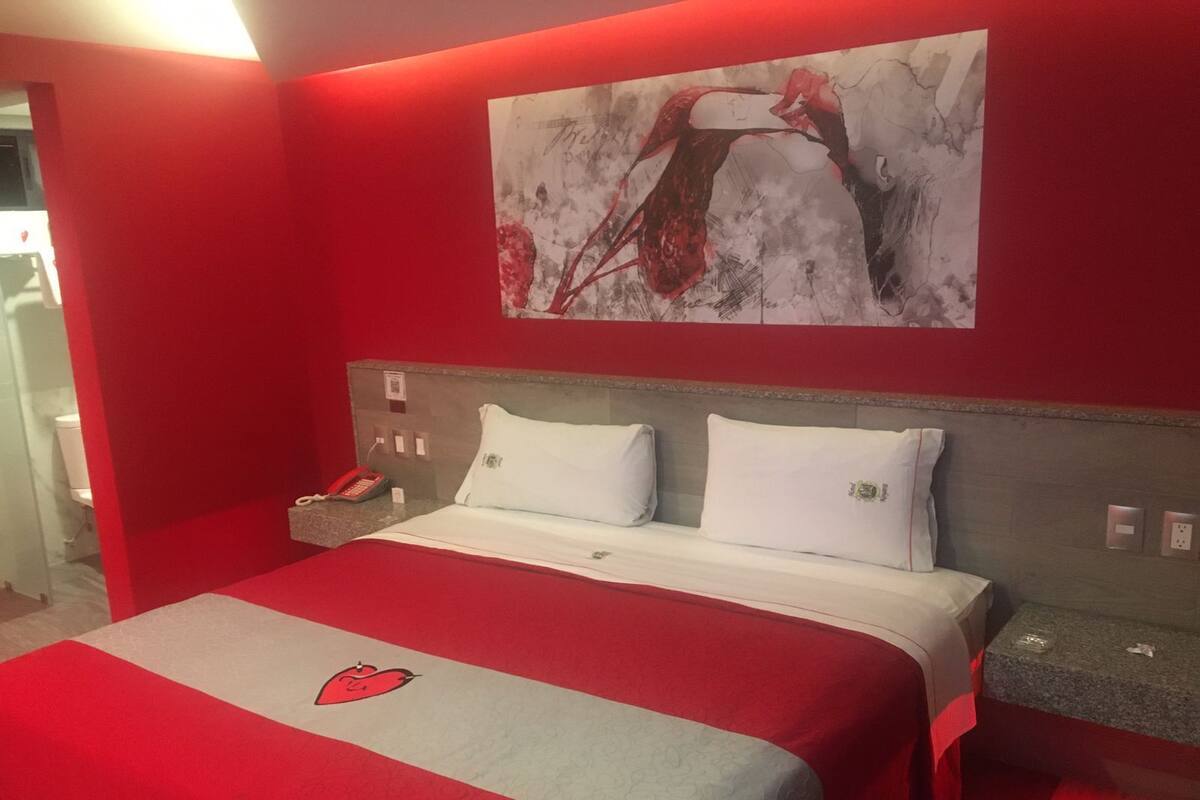 A hotel room with a red and white bedspread, a painting on the wall, and a telephone on the nightstand.