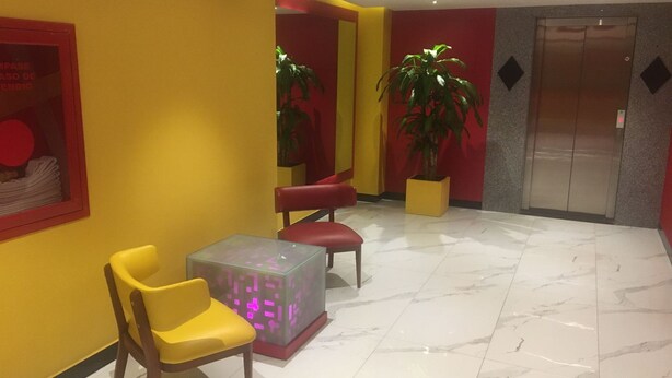 A lobby with yellow walls, a red chair, a glass table, and a potted plant. - Hotel Nayarit - Solo Adultos (Mexico City)