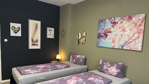Une chambre avec deux lits, une literie à motifs floraux, un mur orné de tableaux et un miroir.