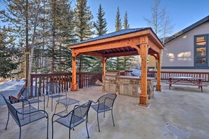 Eine überdachte Terrasse im Freien mit Grill, Steintheke und Metallstühlen.