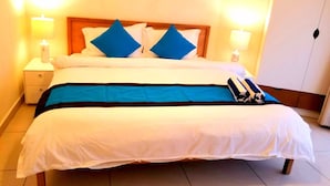 A double bed with a wooden headboard, white bedding, and blue accent pillows. There are two bedside tables with lamps and a small nightstand.