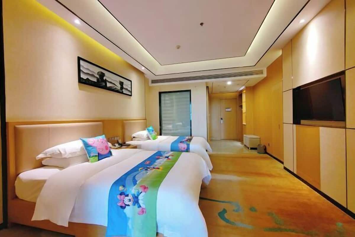 Ein Hotelzimmer mit zwei Betten, einem Fernseher und einem Flur, der zu einem Badezimmer führt.