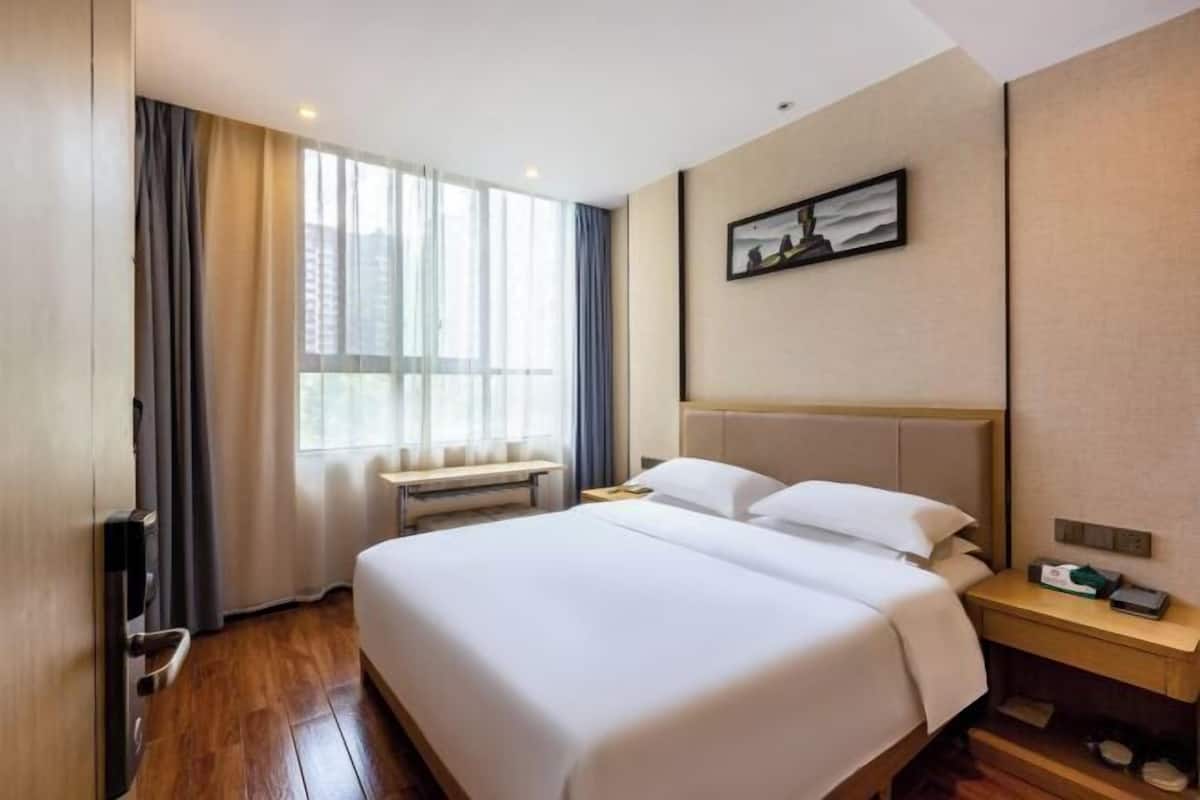 Ein Hotelzimmer mit einem großen Bett, einem Nachttisch, einem Fenster mit Vorhängen und einem Bild an der Wand.