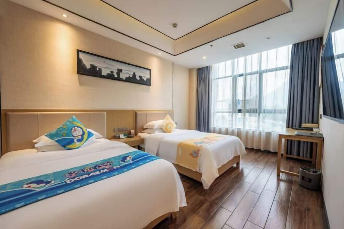 Ein Hotelzimmer mit zwei Betten, einem Stadtbildgemälde, einem Vorhangfenster und Holzboden.