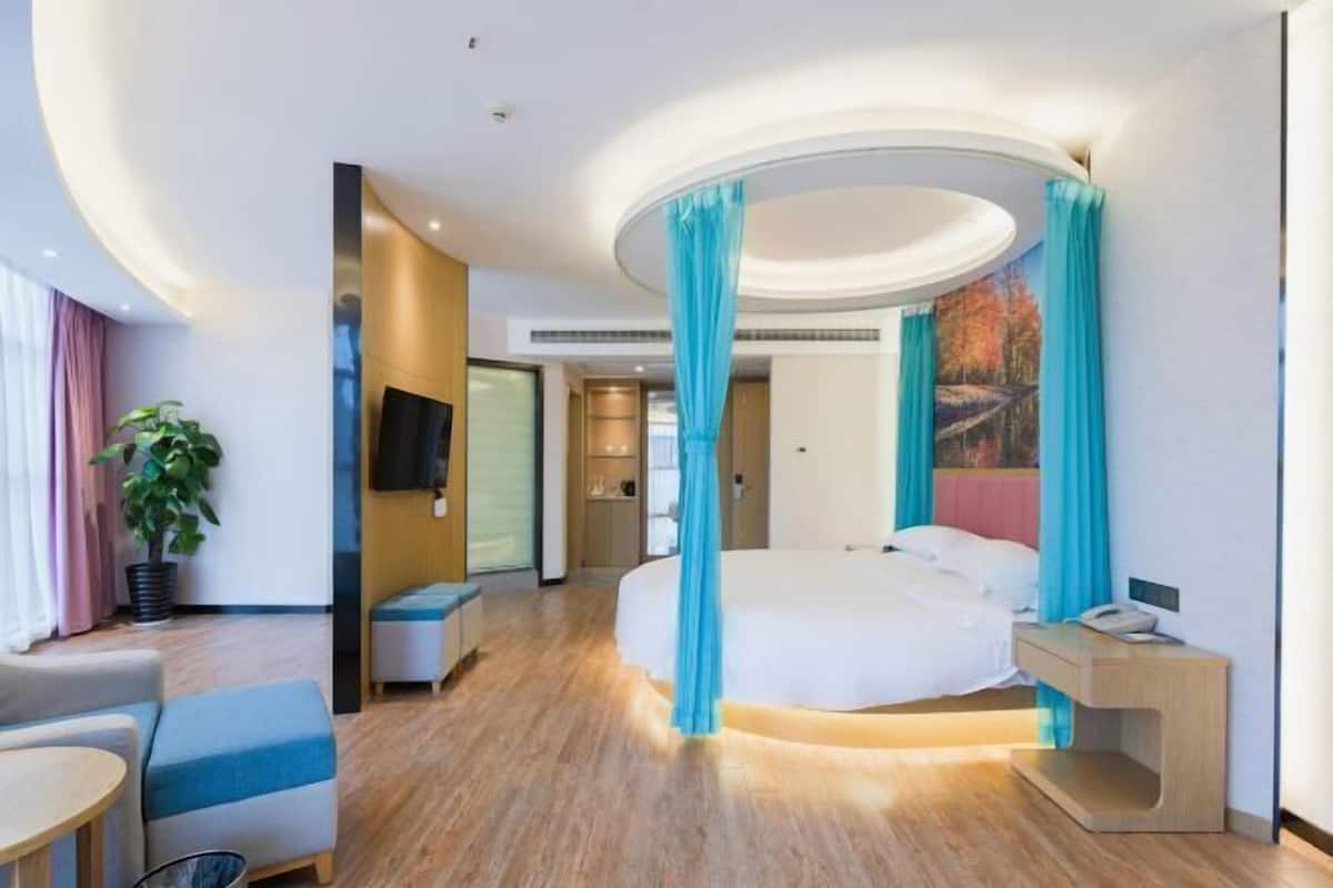 Ein modernes Hotelzimmer mit gewölbter Decke, einem Himmelsbett, einem Nachttisch, einem Sessel und einem kleinen Tisch.