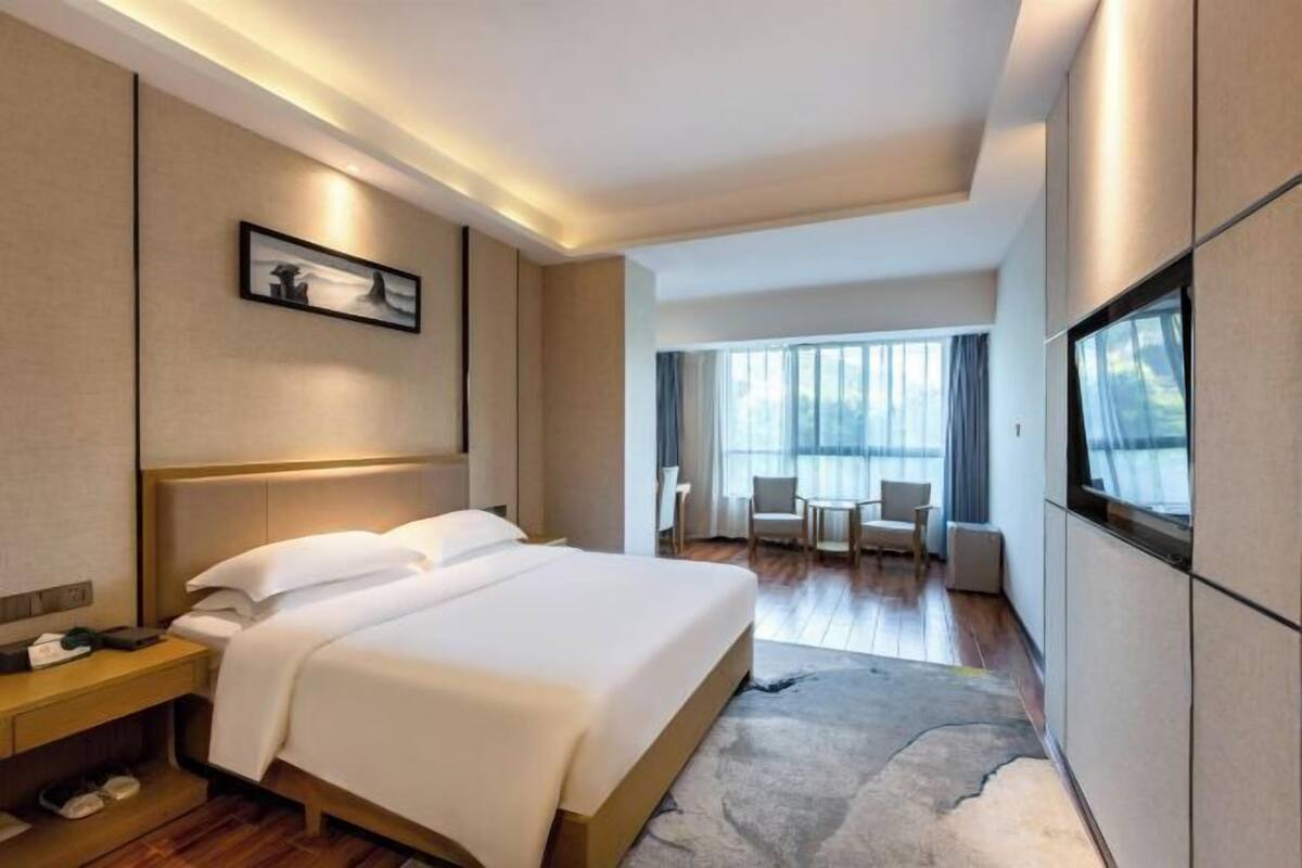 Ein modernes Hotelzimmer mit einem großen Bett, einem Schreibtisch, einem Fernseher und Blick ins Freie.
