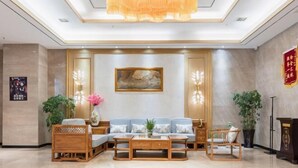 Un hall d’entrée avec un canapé, une table basse, des chaises en bois, un tableau et un lustre.